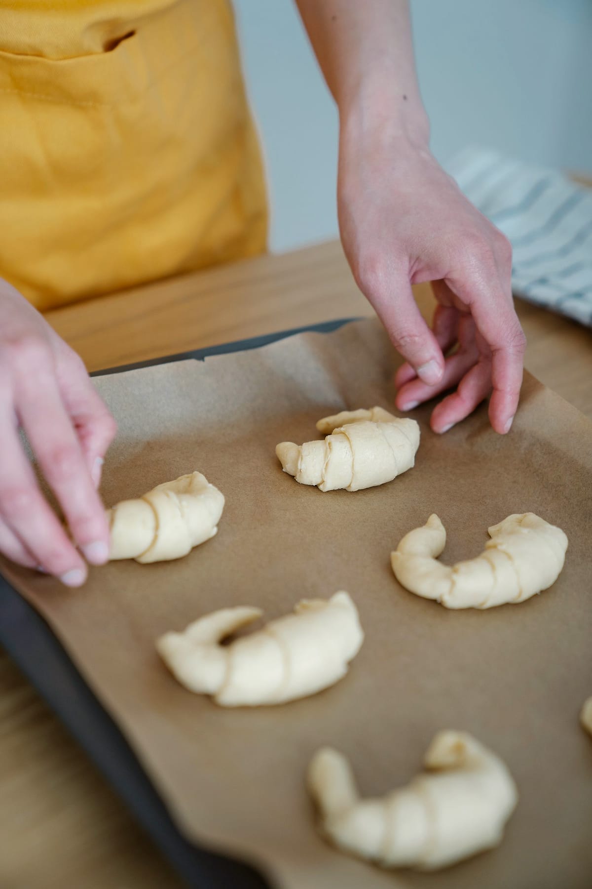 Hands shape croissants on a baking tray lined with paper.
