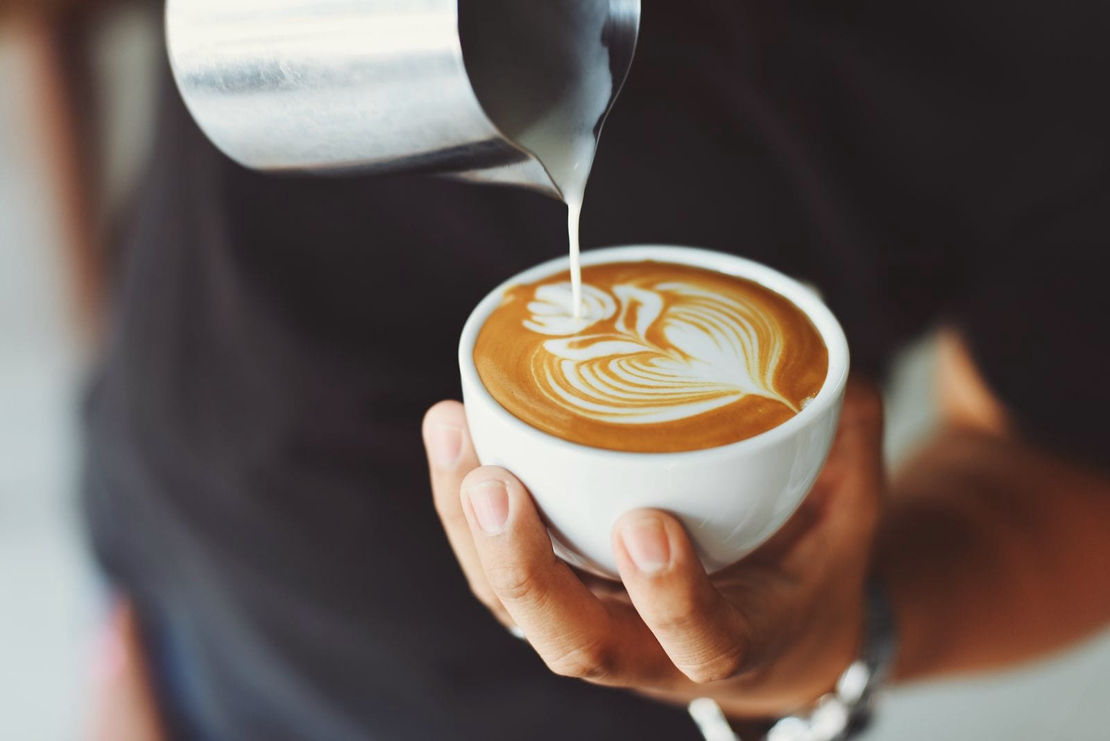 Milk is poured into a white cup, finishing a leaf of latte art.