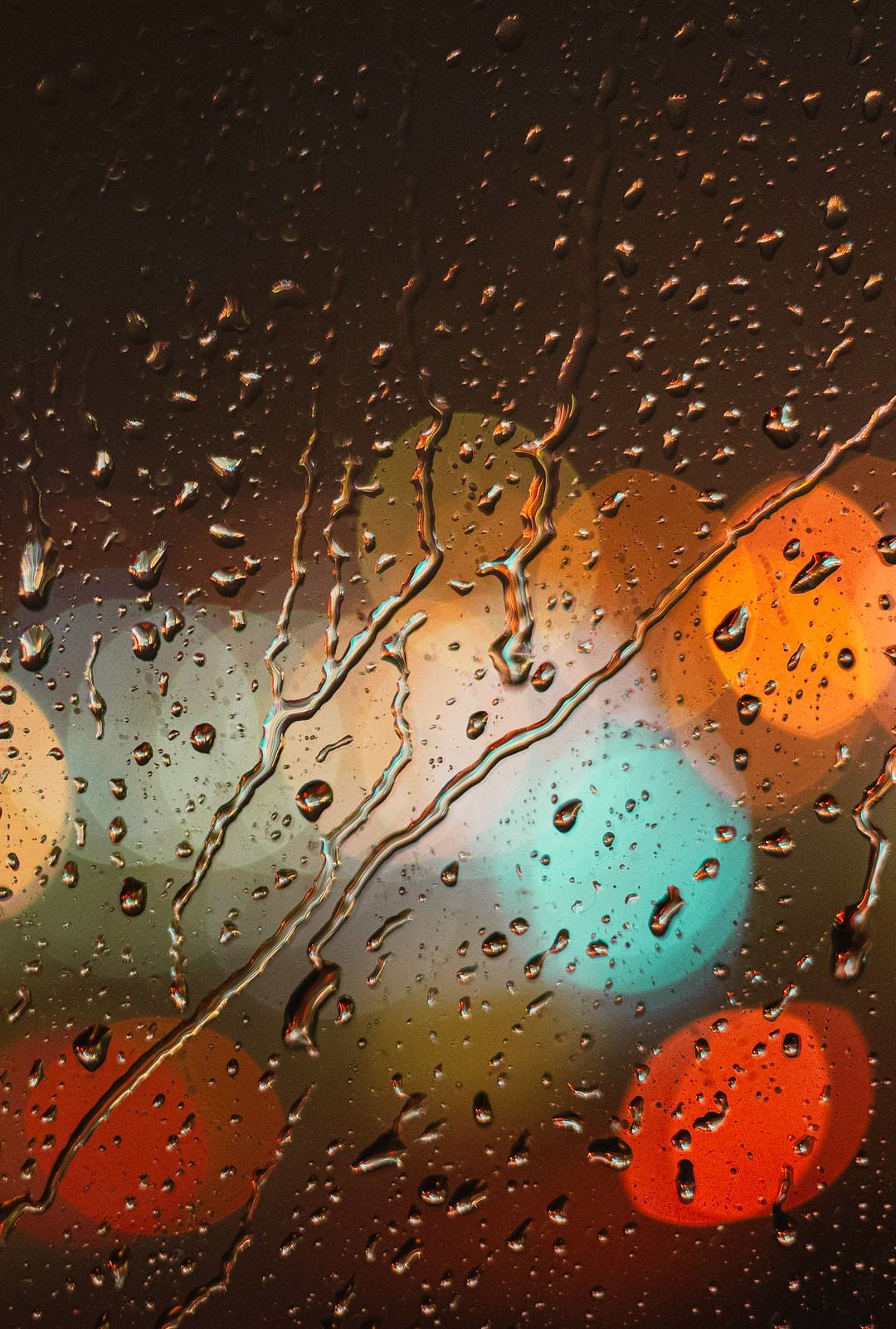 Raindrops on a window pane, with warm city lights blurred behind them.