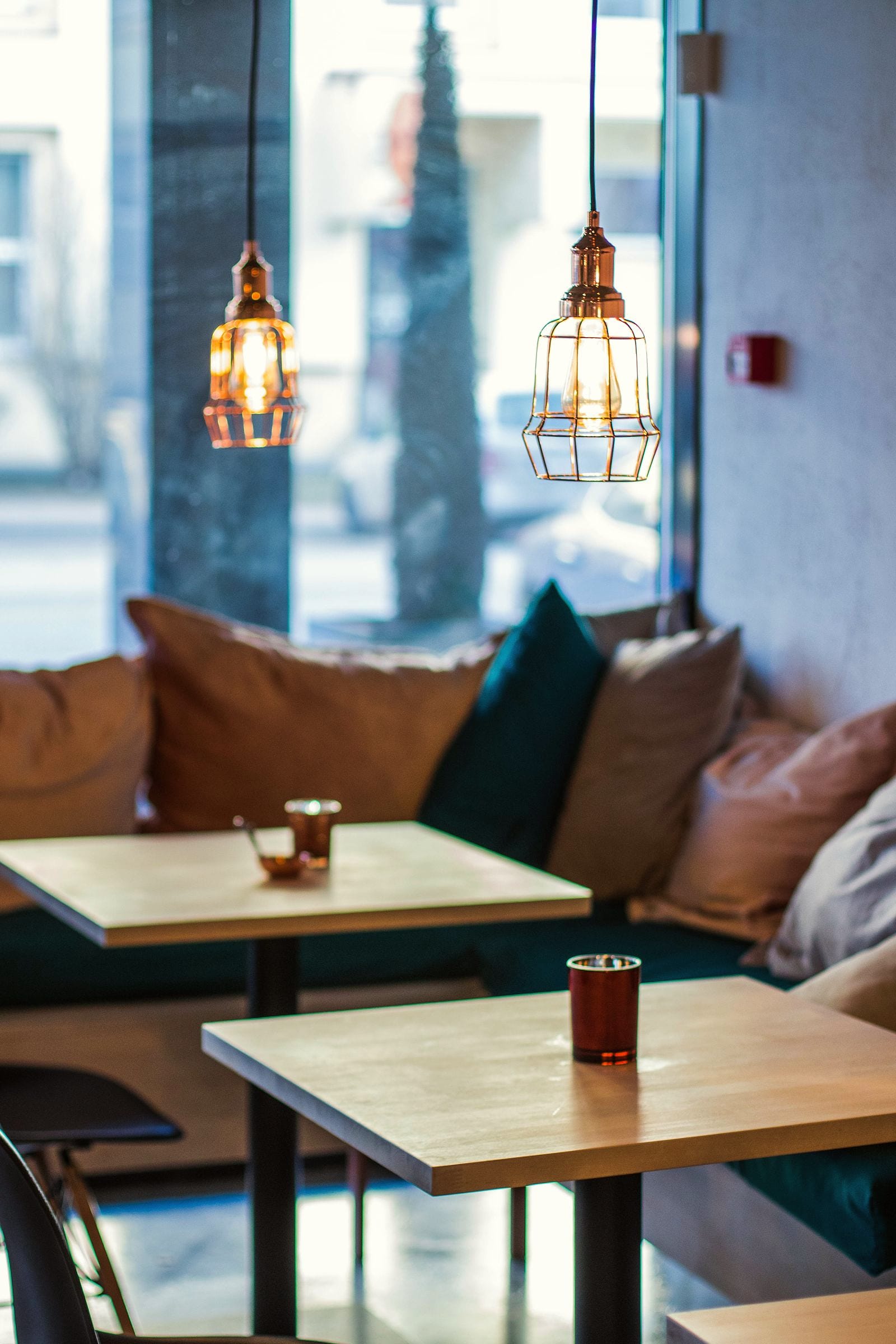 Brass pendant lamps hang over small tables and a cushioned window seat.